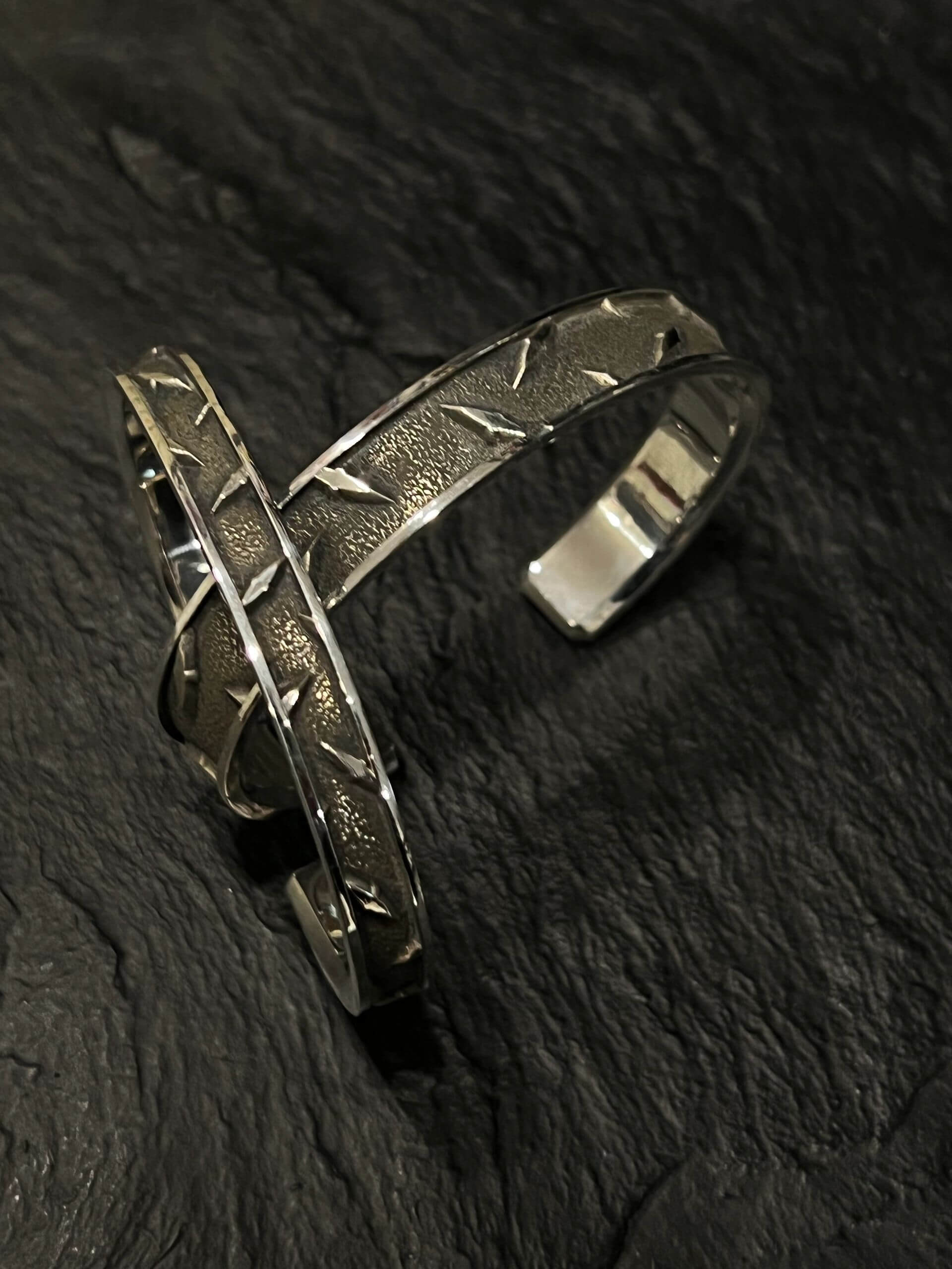 Close-up of a rustic metal bracelet on a dark textured surface.