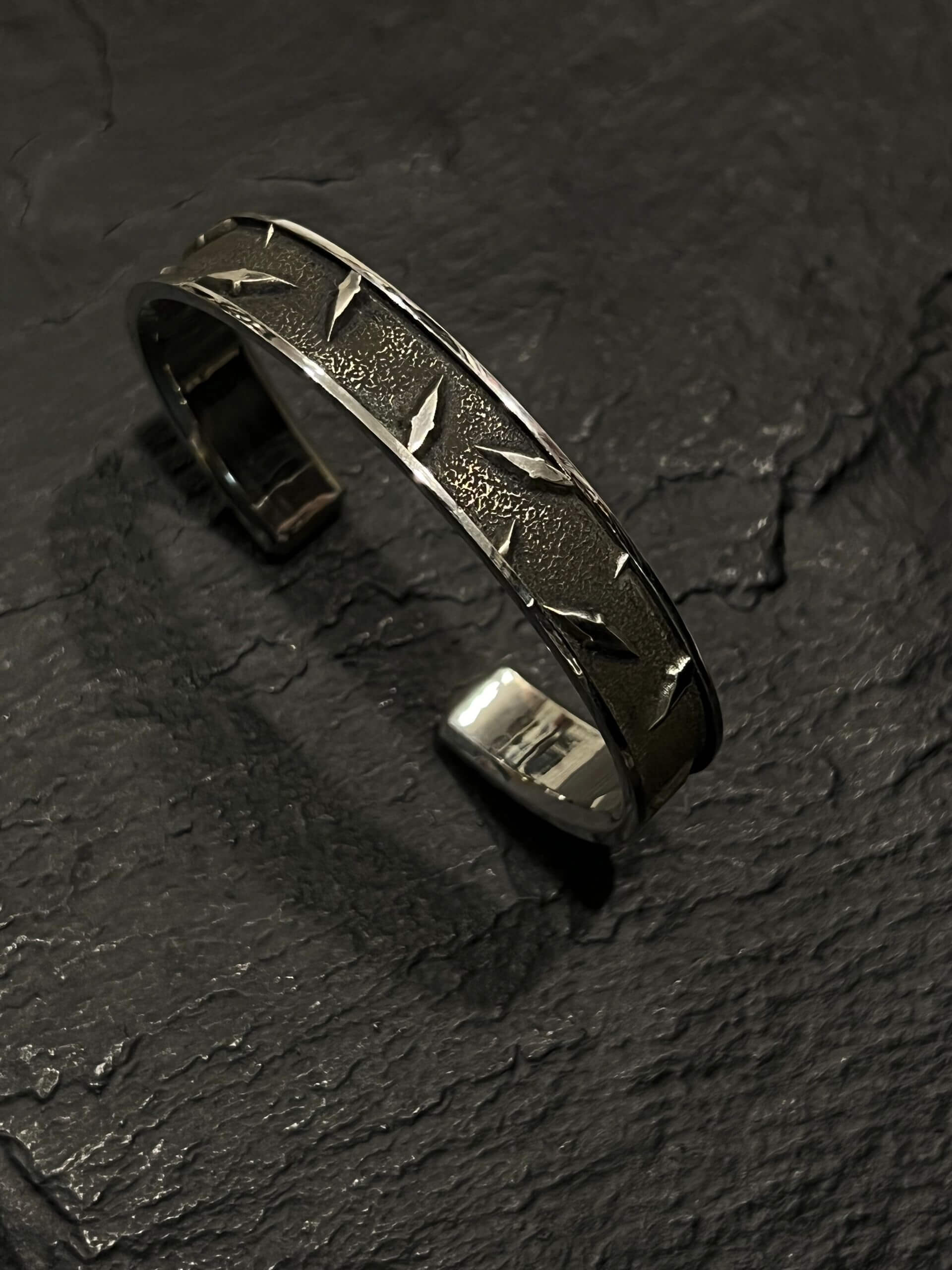 Silver cuff bracelet with star engravings on a dark surface.
