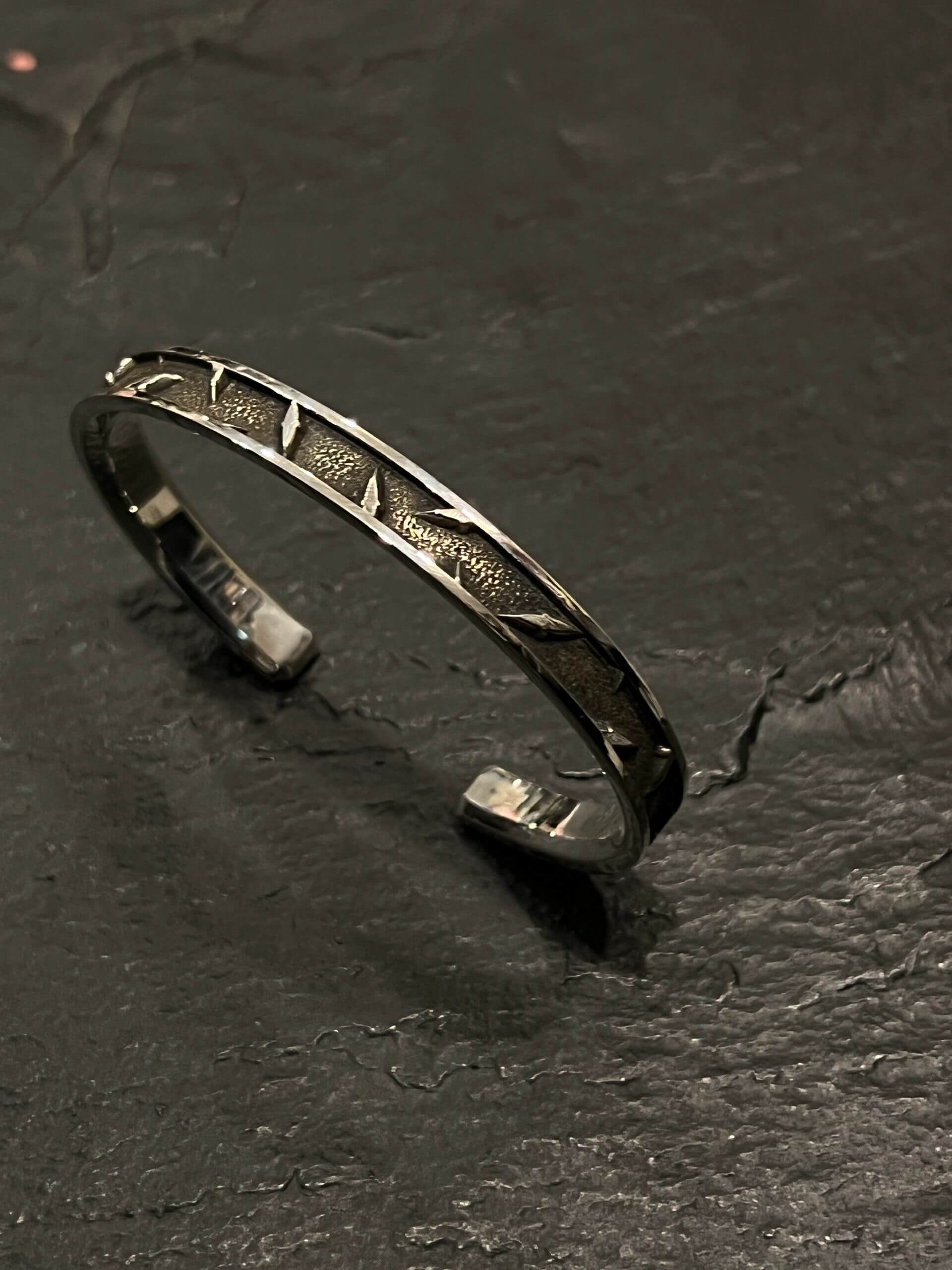 A silver cuff bracelet with geometric patterns on a dark surface.