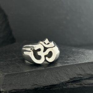 A silver ring featuring the Om symbol on a dark surface.