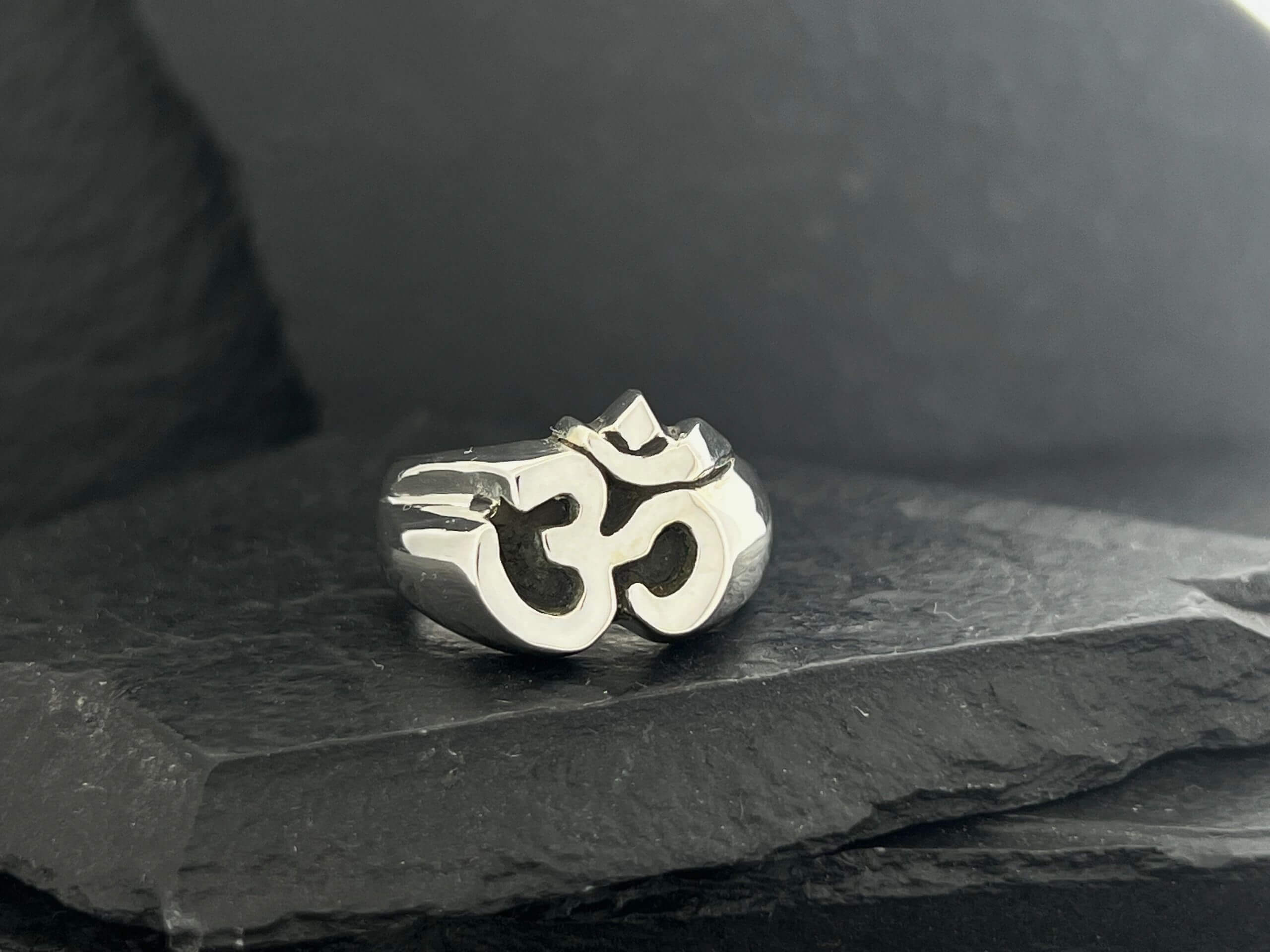 A silver ring featuring the Om symbol on a dark surface.