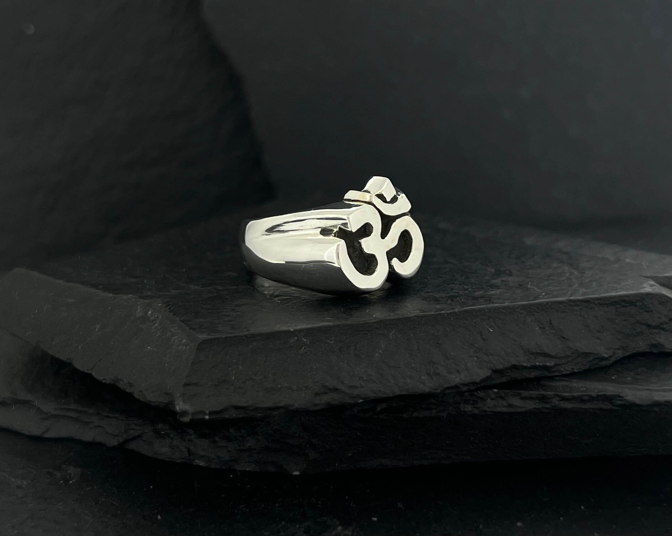 Silver ring featuring a prominent Om symbol on a dark background.