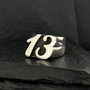A silver ring featuring the number 13 on a dark surface.