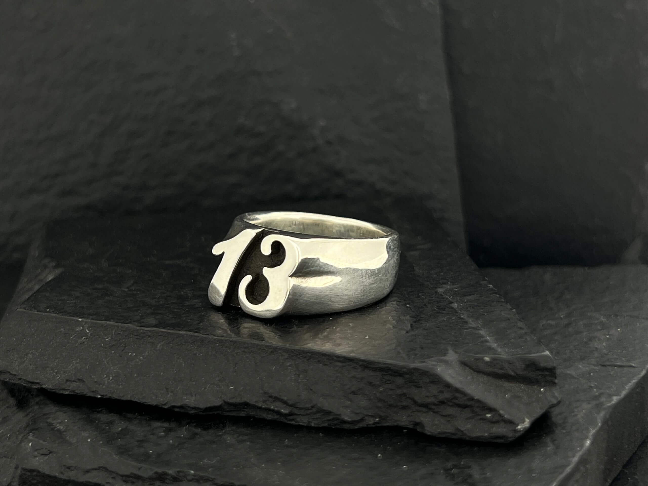 Silver ring featuring the number 13 on a dark stone surface.