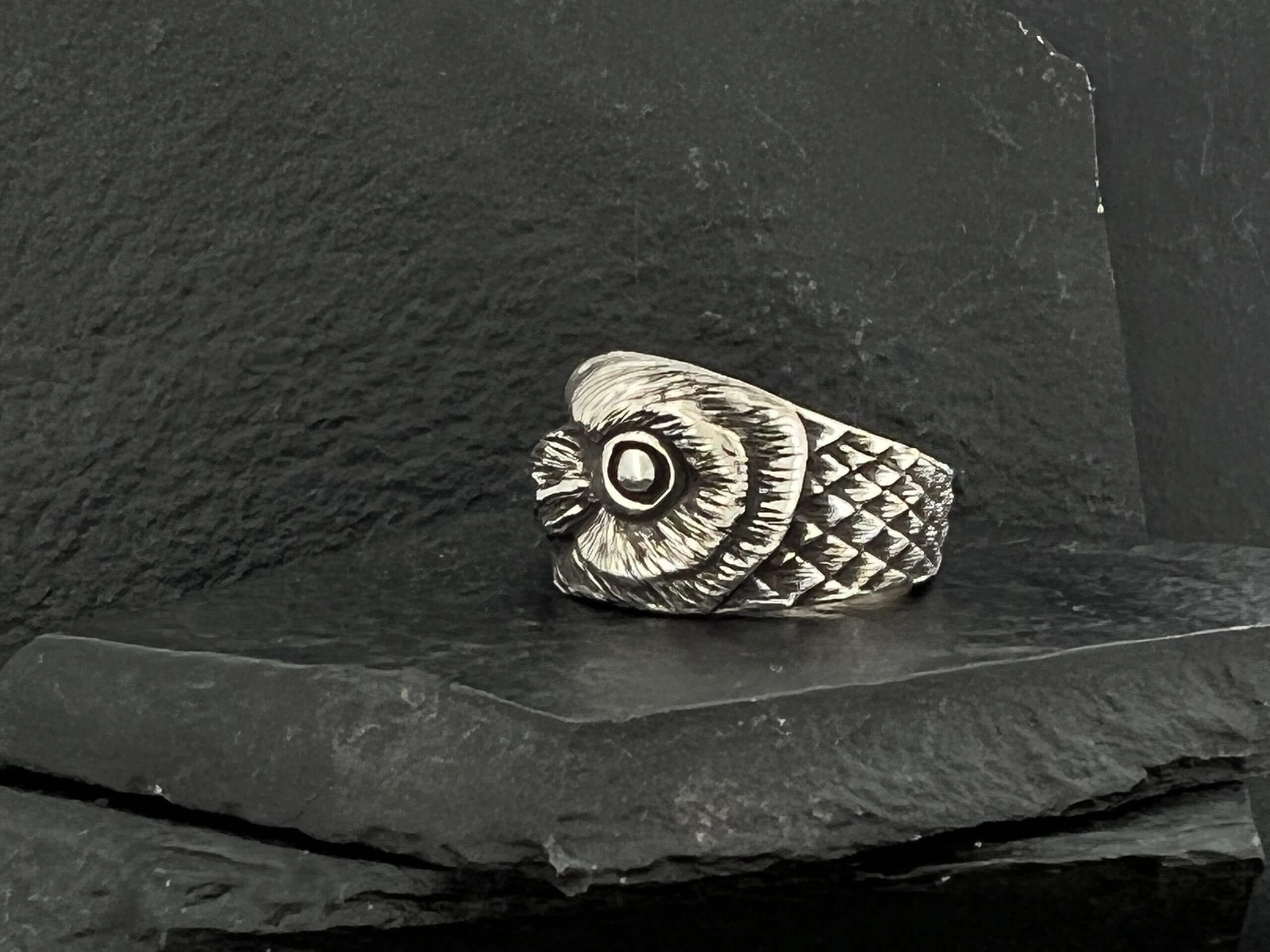A detailed silver owl-shaped ring on a dark stone surface.