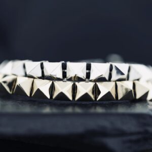 Close-up of silver pyramid-studded bracelets on a dark surface.