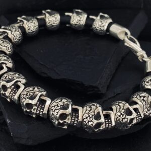 Silver bracelet with skull designs on a dark surface.