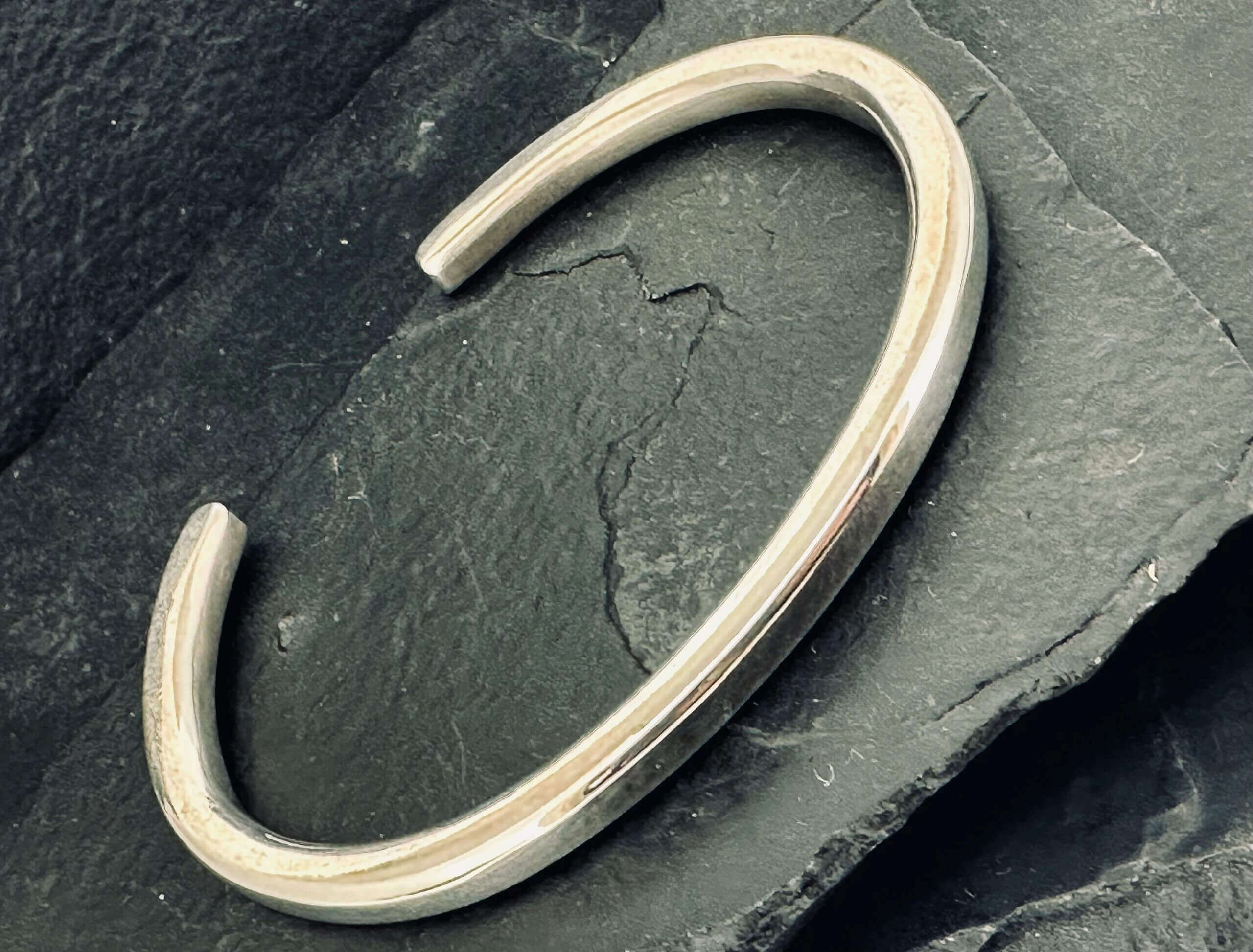 A sleek silver cuff bracelet on a dark slate surface.