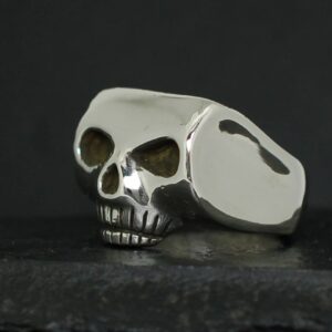 A metallic skull-shaped ring with dark eye sockets on a dark surface.