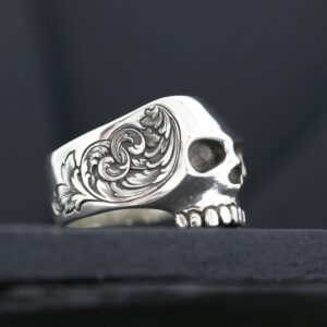 A detailed silver skull ring with intricate floral engravings.