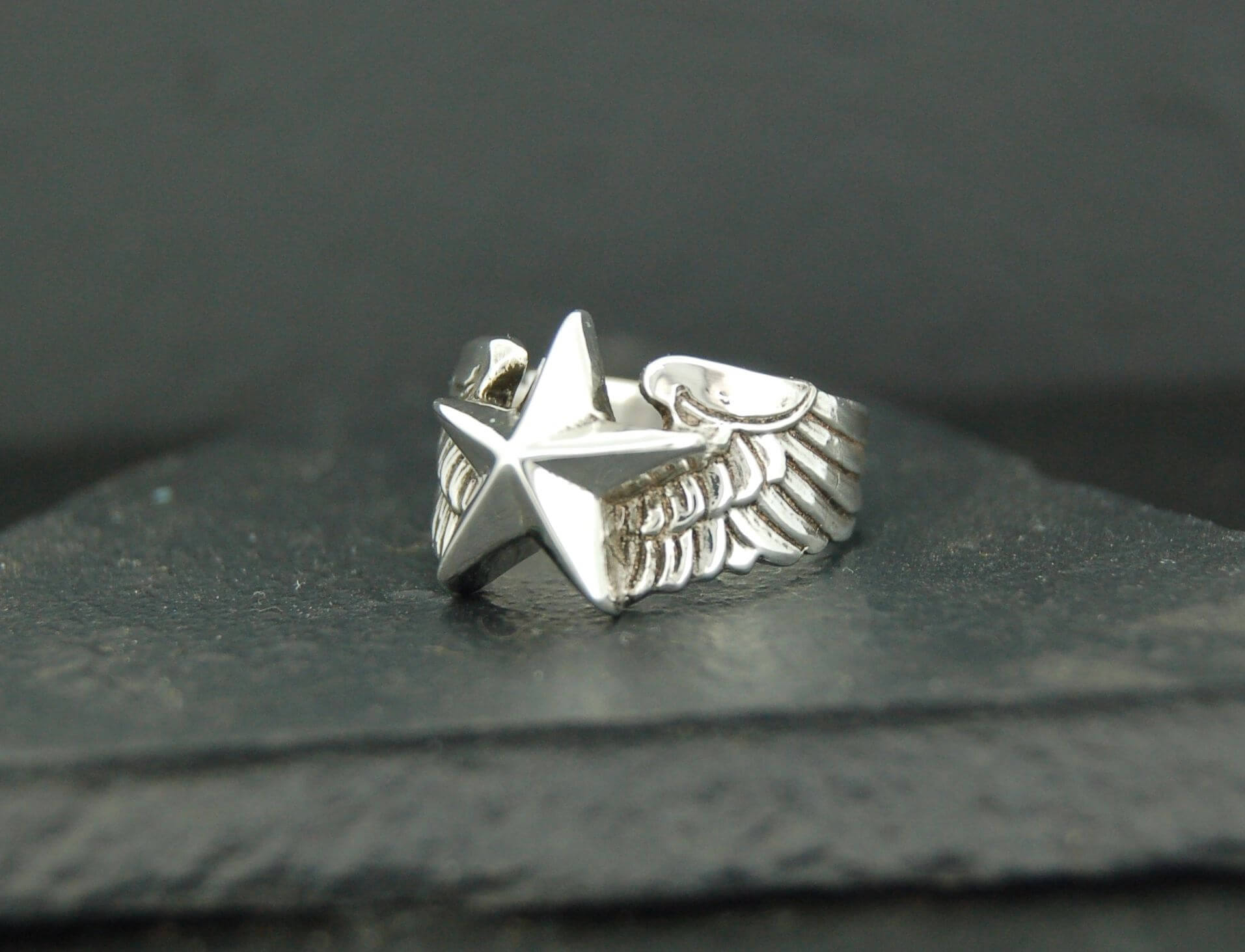 Silver ring with a star and wing design on a dark surface.
