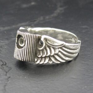 Silver ring with wing design and screw detail on a dark surface.