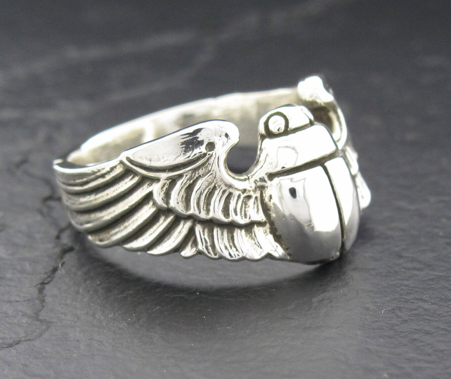 Close-up of a silver ring with detailed wing and grenade design.