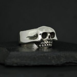Silver skull-shaped ring on a black surface.