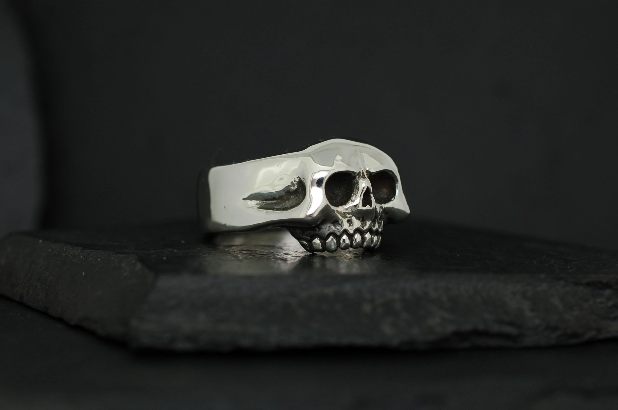 Silver skull-shaped ring on a black surface.
