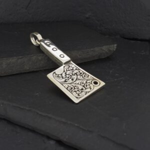 A silver axe-shaped pendant with intricate designs on a dark background.