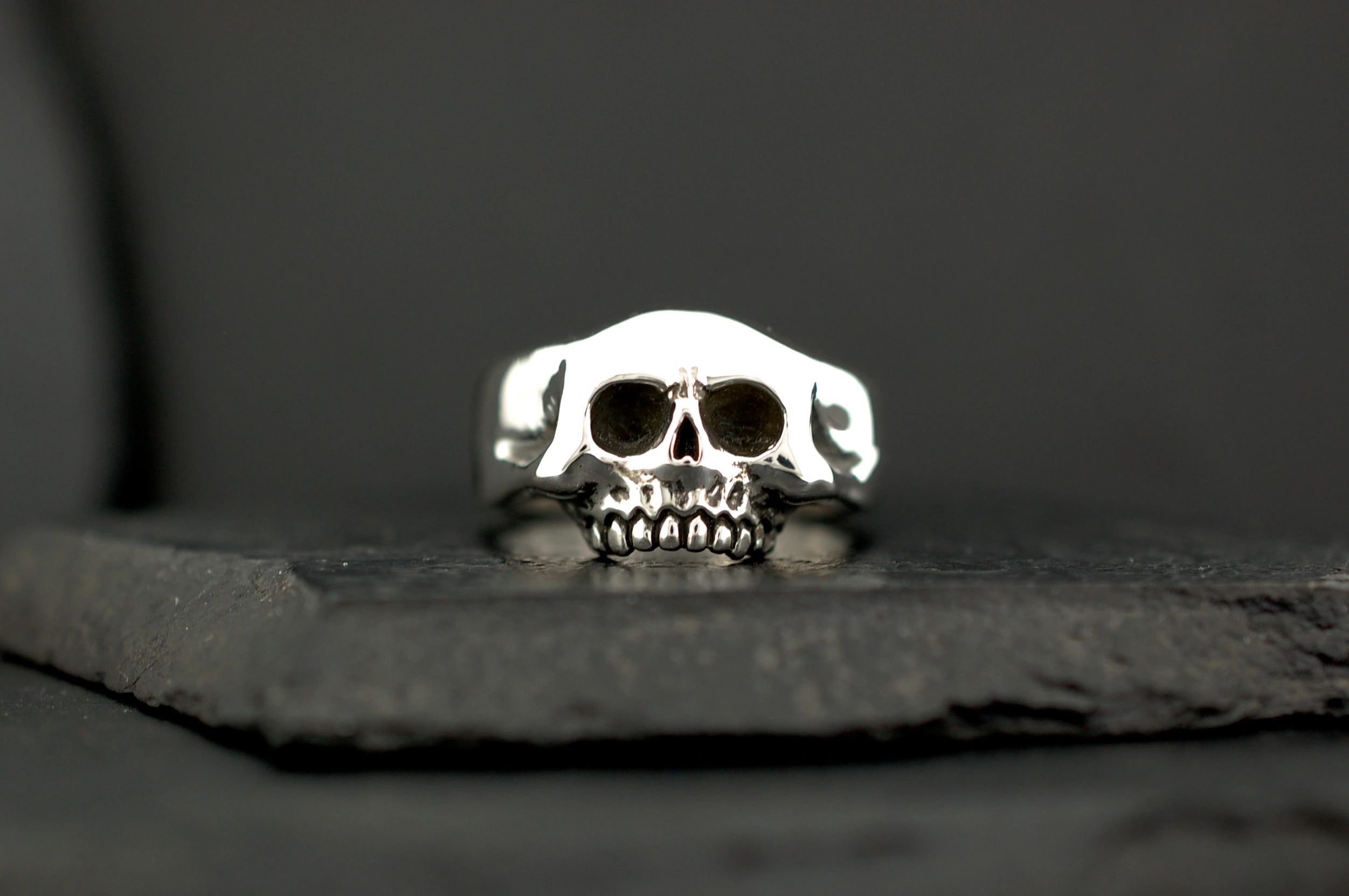 Close-up of a silver skull ring on a dark surface.