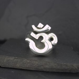 A silver Om symbol pendant on a dark surface.