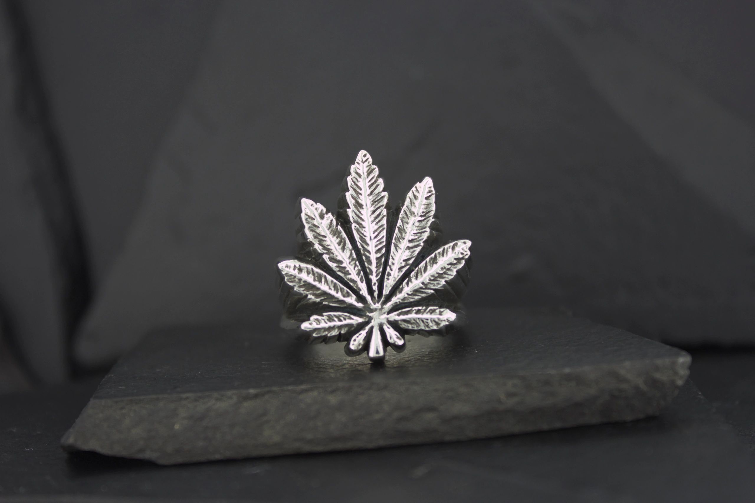 A silver cannabis leaf-shaped pendant on a dark surface.