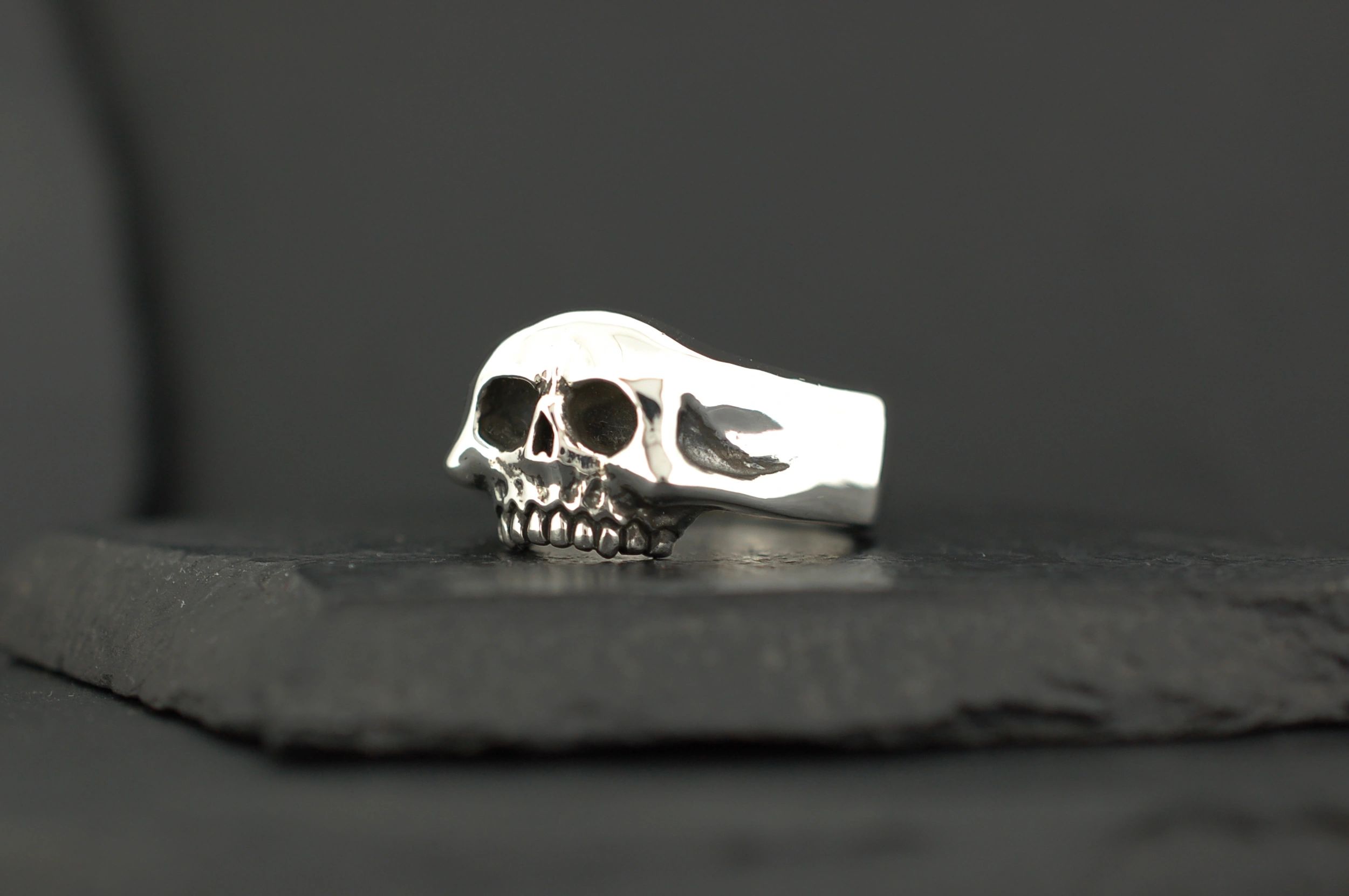 A silver skull-shaped ring on a dark surface.