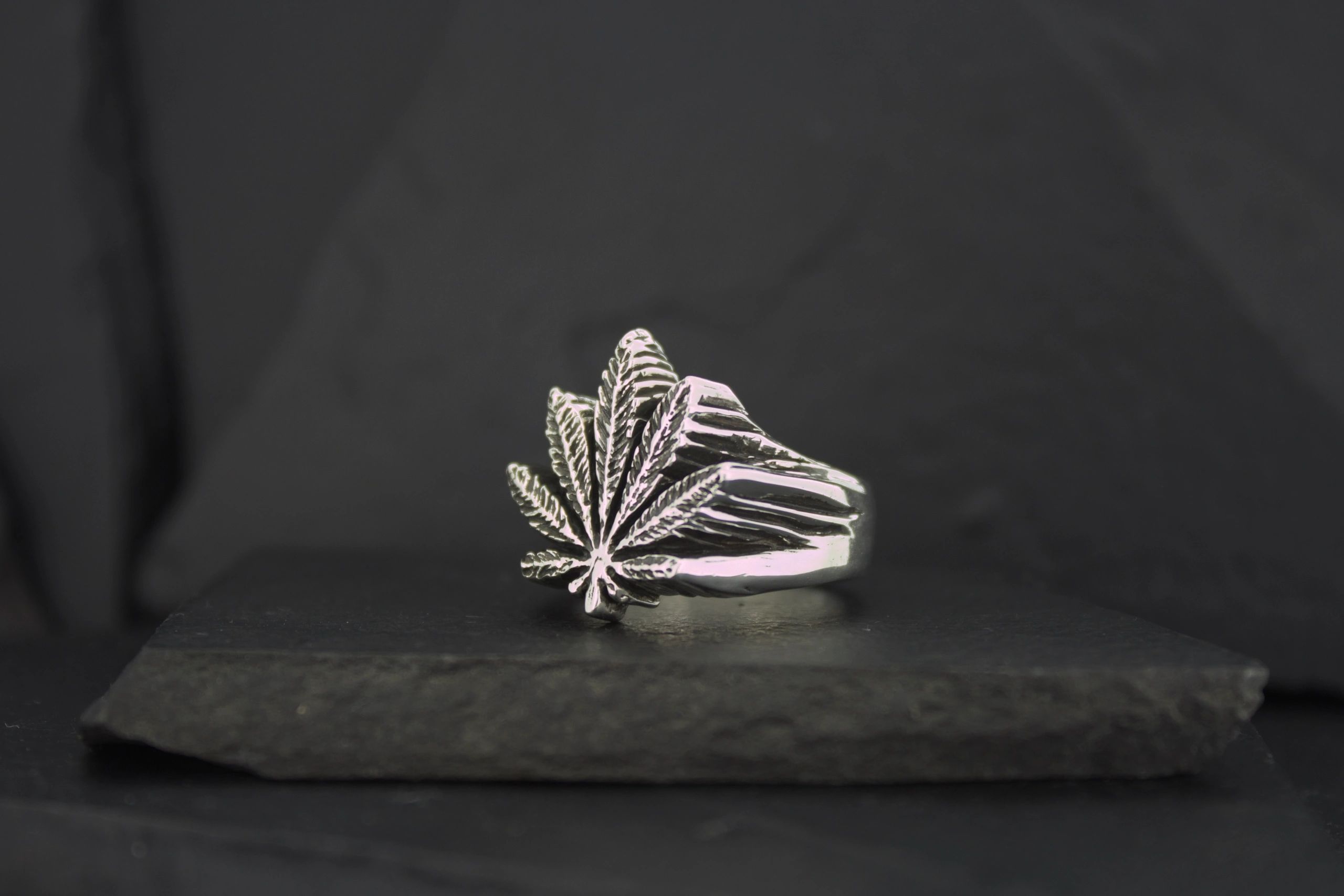 Silver ring with a stylized leaf design on a dark surface.