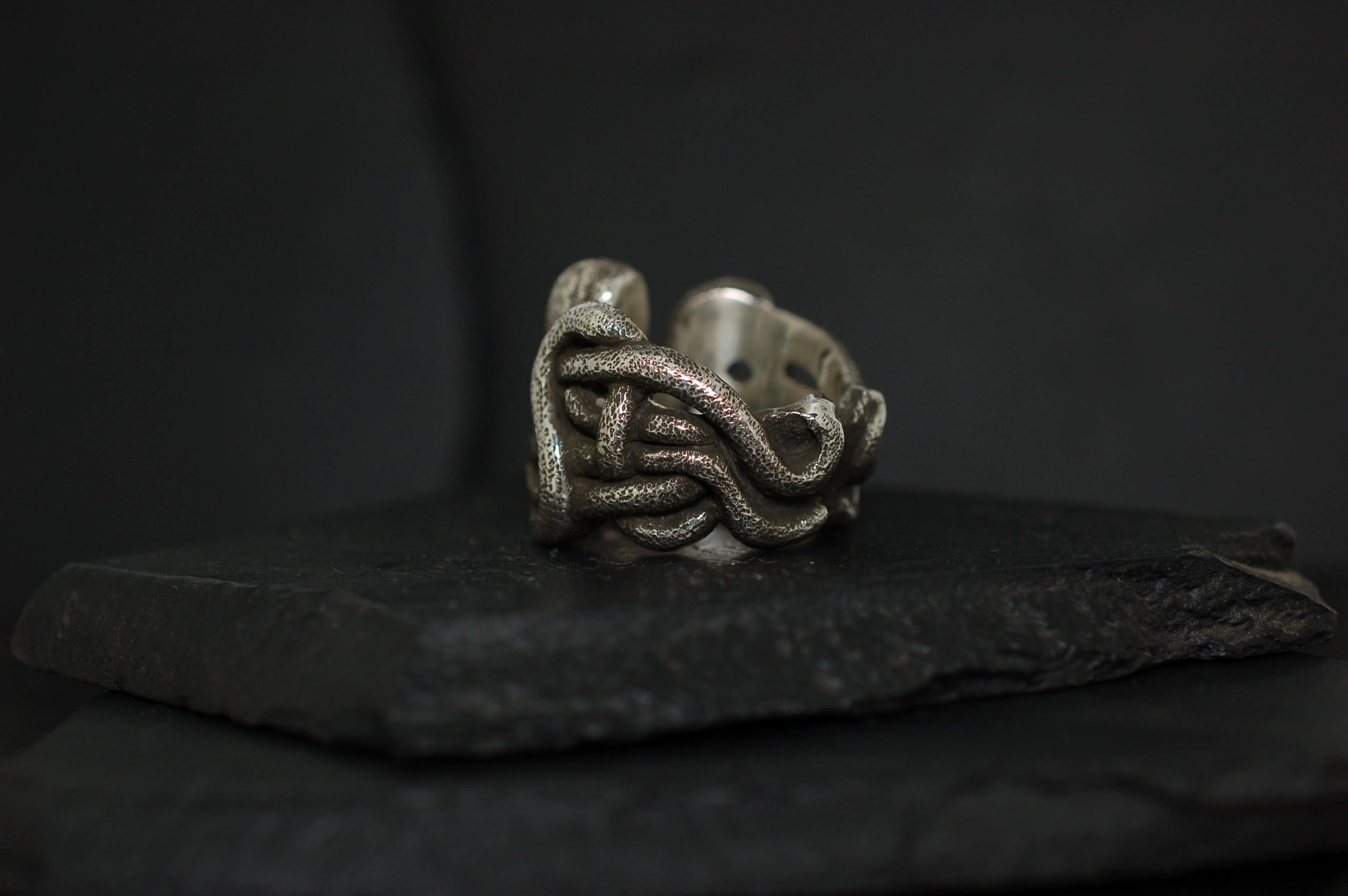 Intricate silver ring with a twisted knot design on a dark surface.