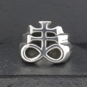 Silver ring with an intricate, symbolic design on a dark background.