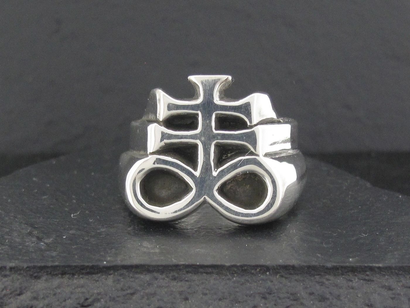 Silver ring with an intricate, symbolic design on a dark background.