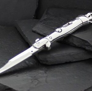 A sleek silver automatic knife with a pointed blade on dark slate stones.
