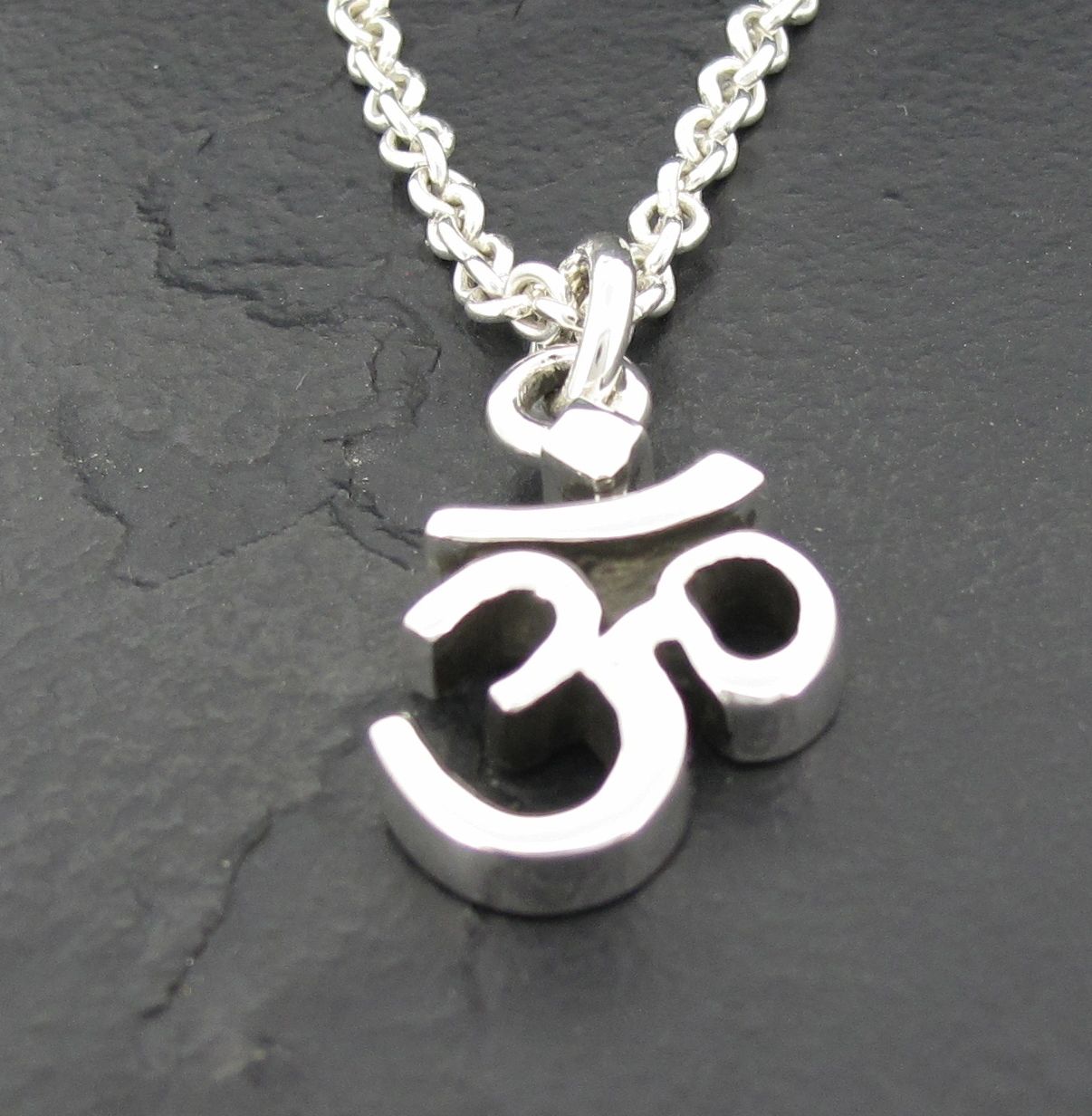 Silver Om symbol pendant on a chain against a dark background.