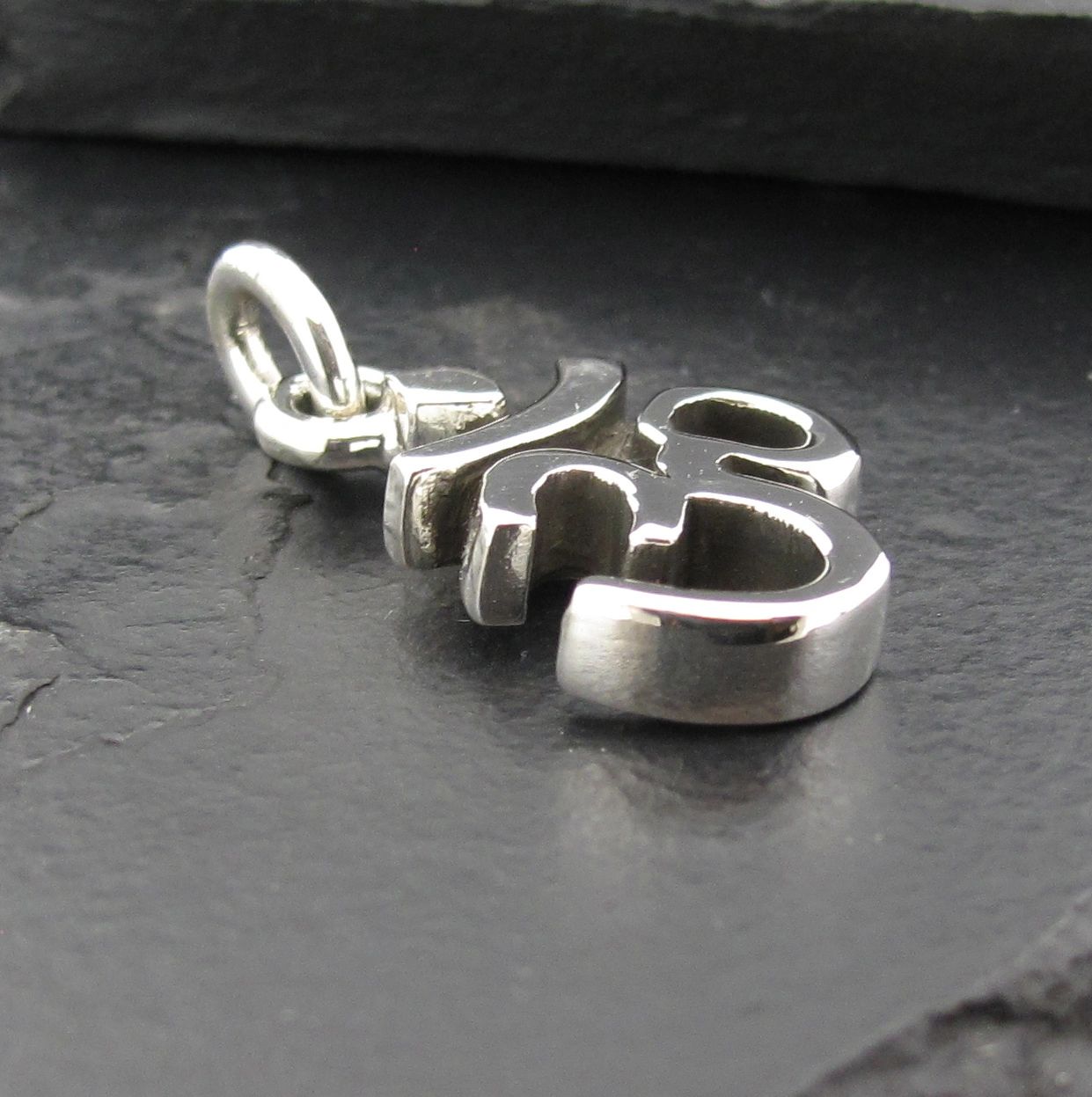 A silver pendant with the word 'this' on a dark surface.
