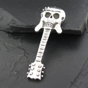 Metal guitar pendant with a skull design on top, placed on a dark stone surface.