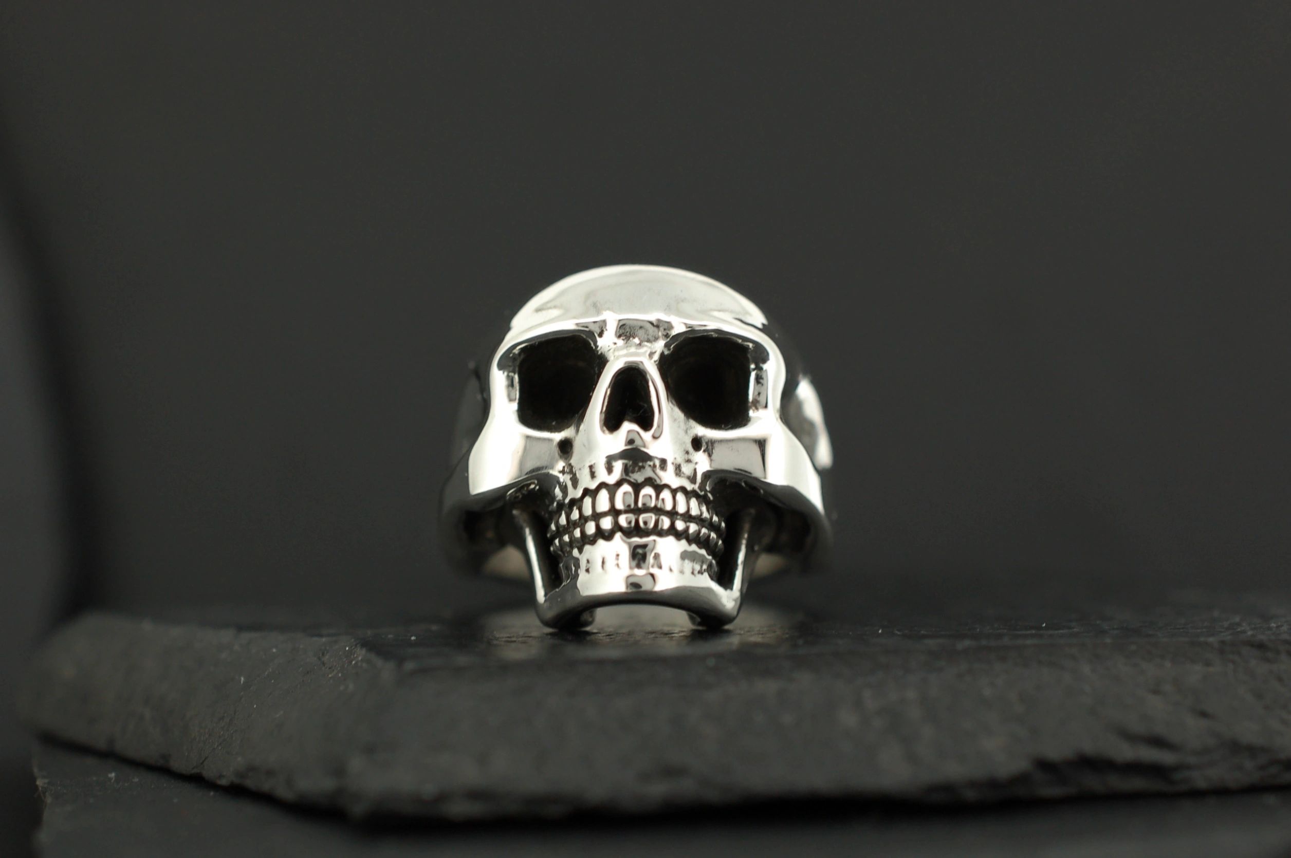 A polished silver skull ring on a dark surface.