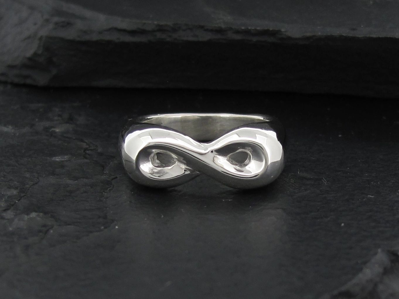 Silver infinity symbol ring on a dark surface.