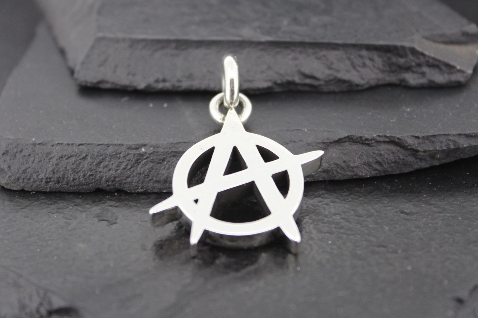 Silver anarchy symbol pendant on a dark textured background.