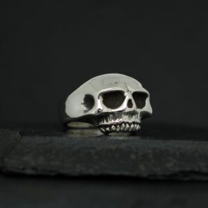 A silver ring shaped like a skull on a dark surface.