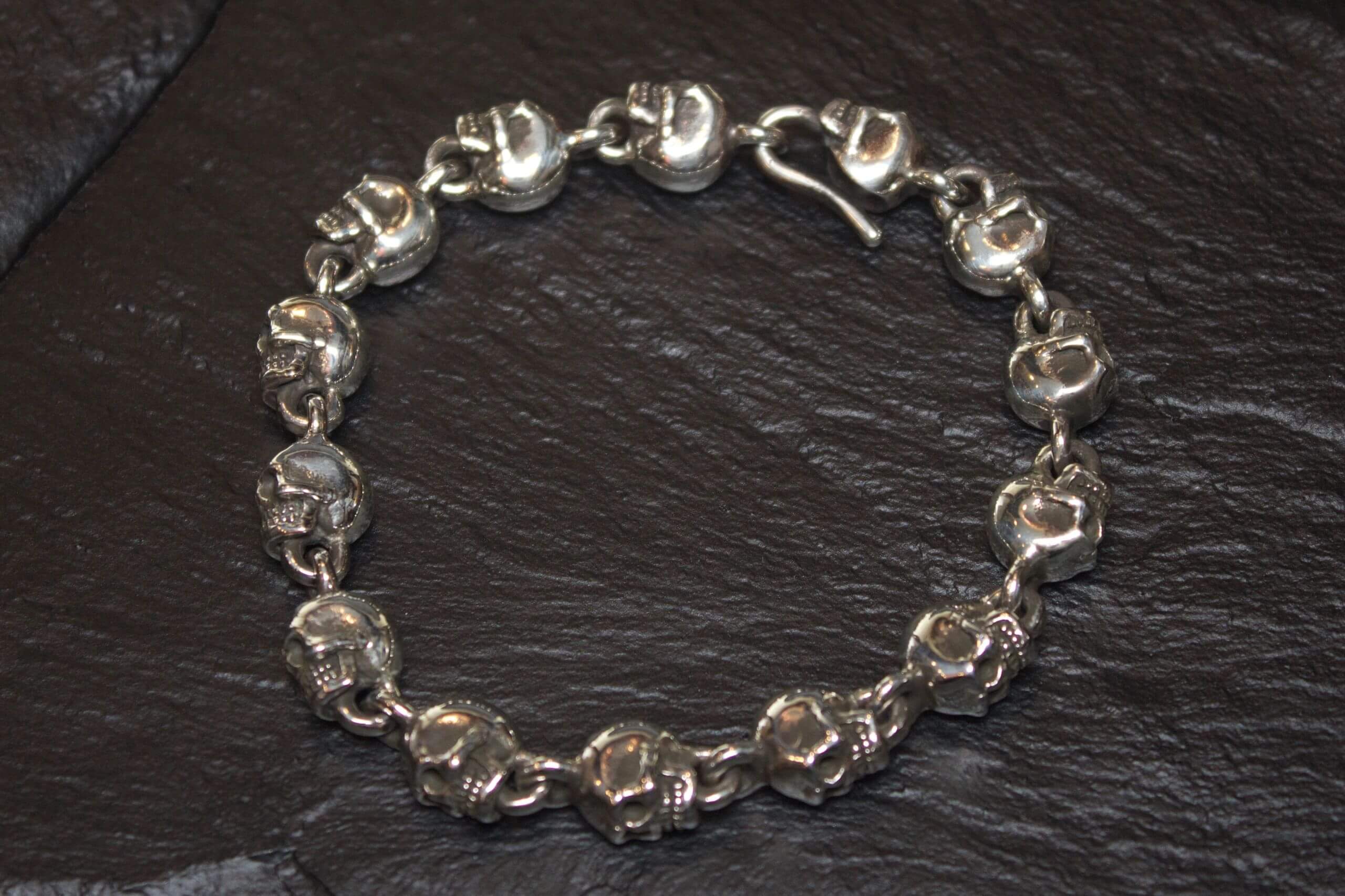Silver skull bracelet with a lobster clasp on a dark background.