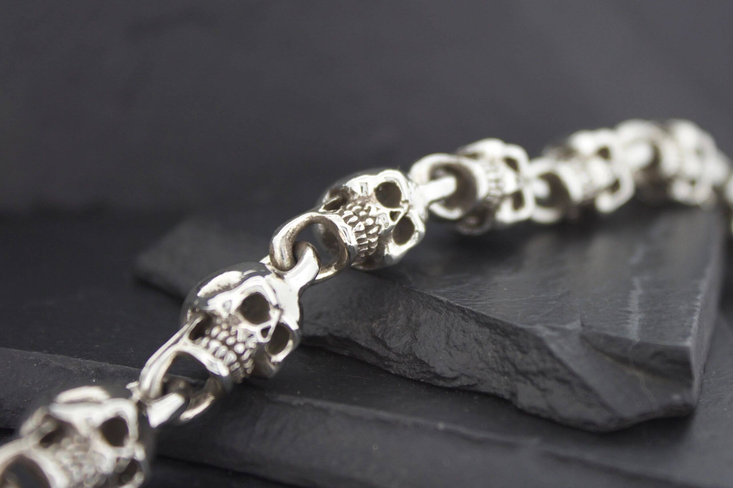 Close-up of a silver skull bracelet on a dark surface.