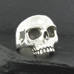 A shiny silver skull ring on a dark surface.