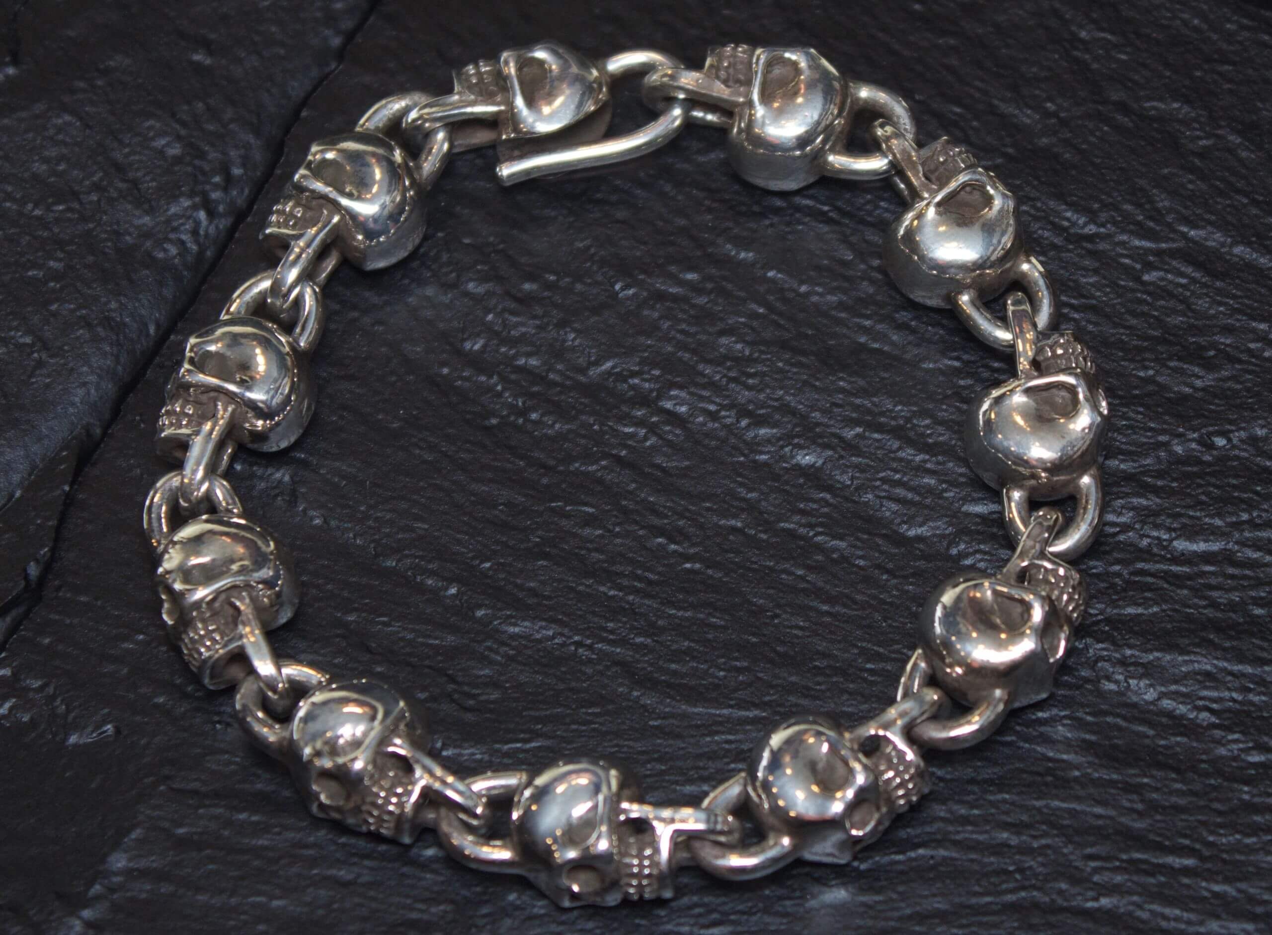 Silver bracelet with skull-shaped links on a dark surface.