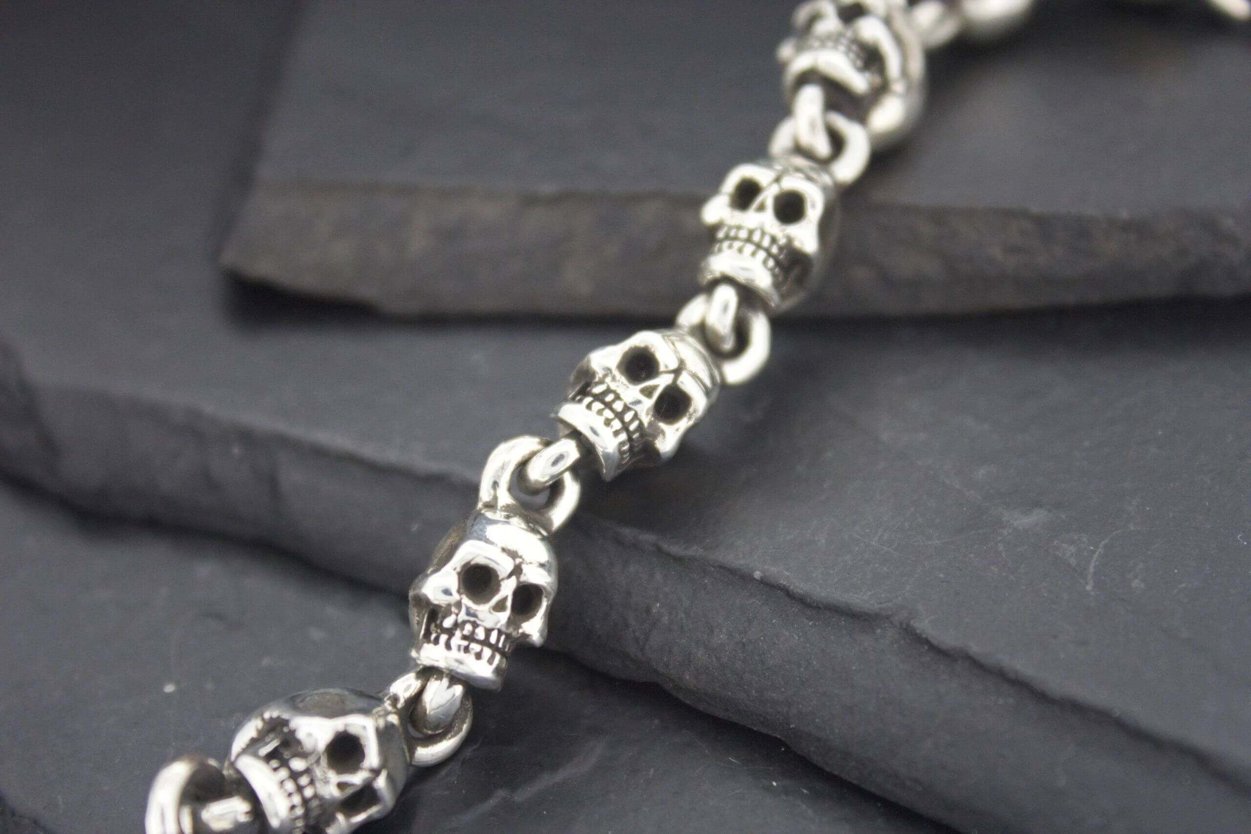 Close-up of a silver skull-themed bracelet on dark stones.