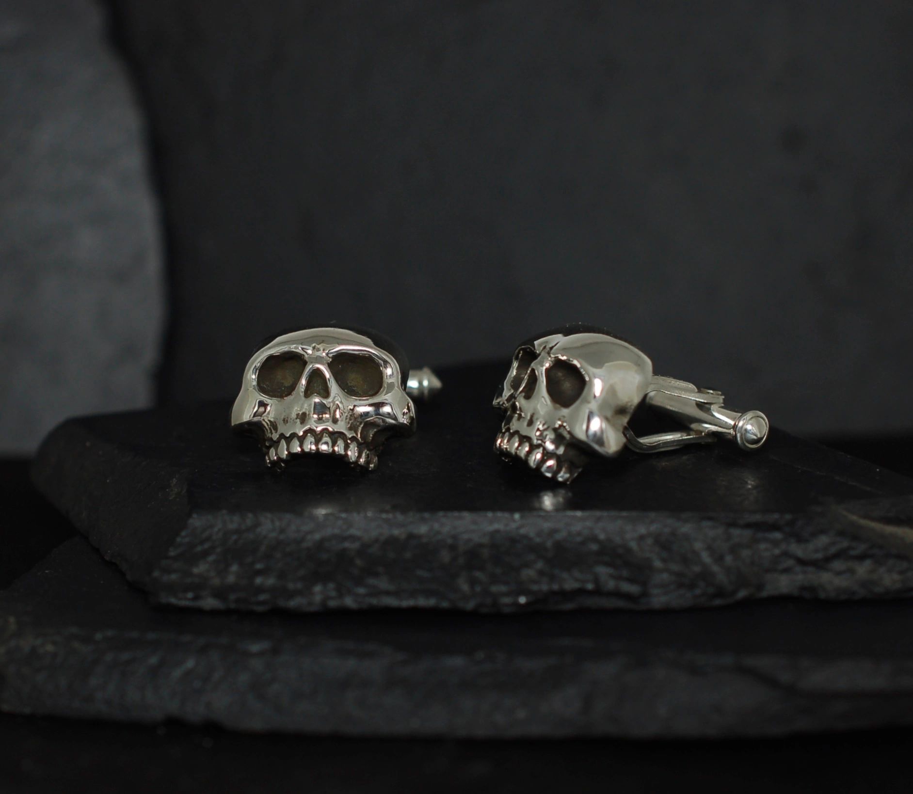Silver skull cufflinks on a dark surface.