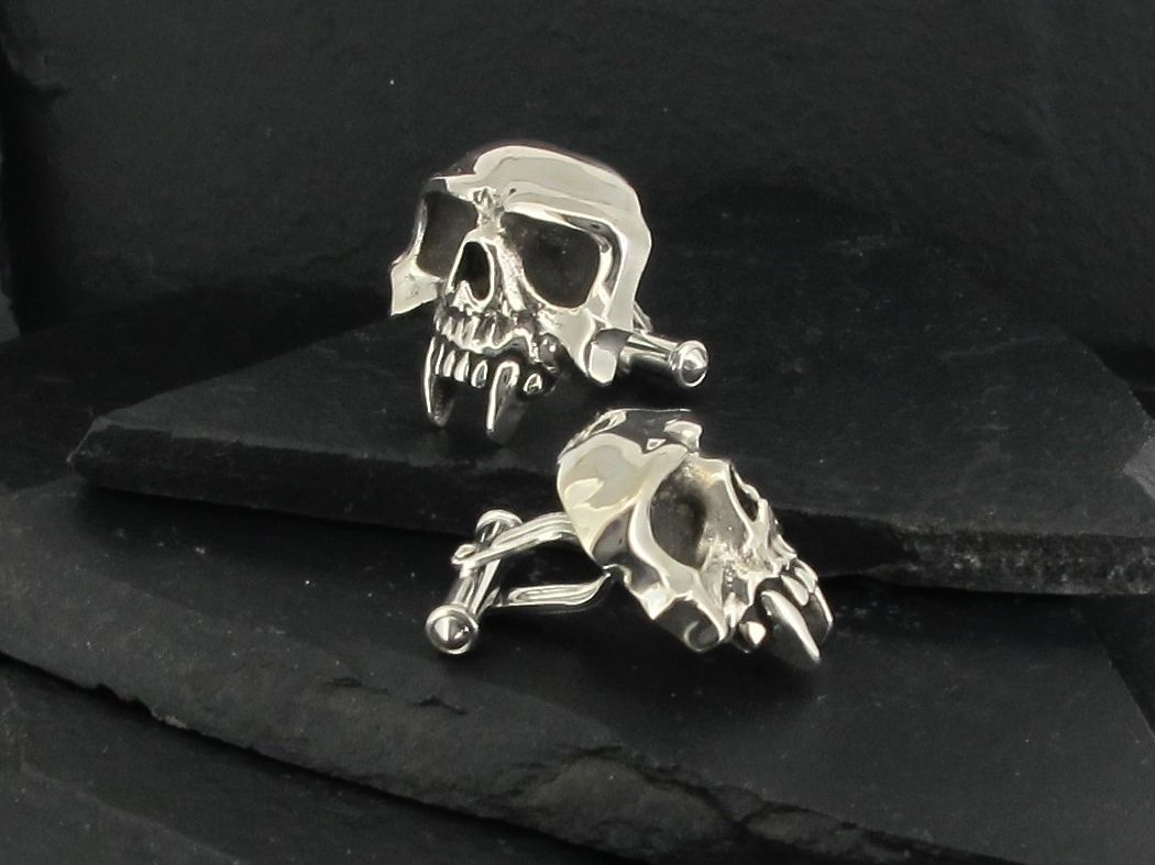 Silver skull-shaped earrings with a dark background.