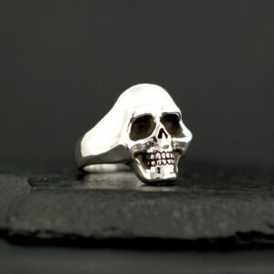 Silver skull ring with detailed features against black background.