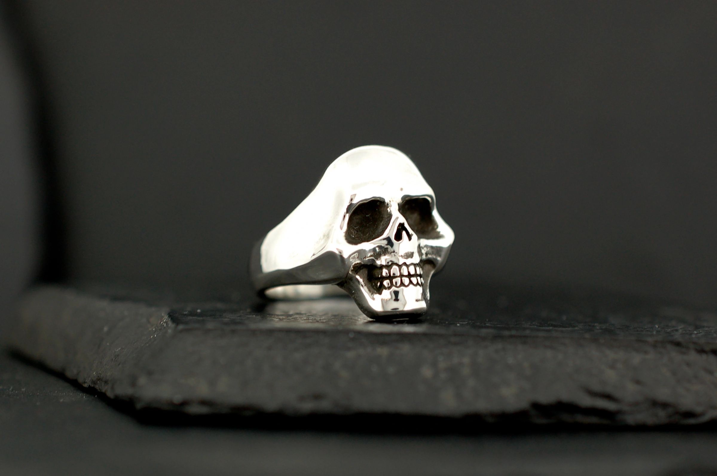 Silver skull ring with detailed features against black background.