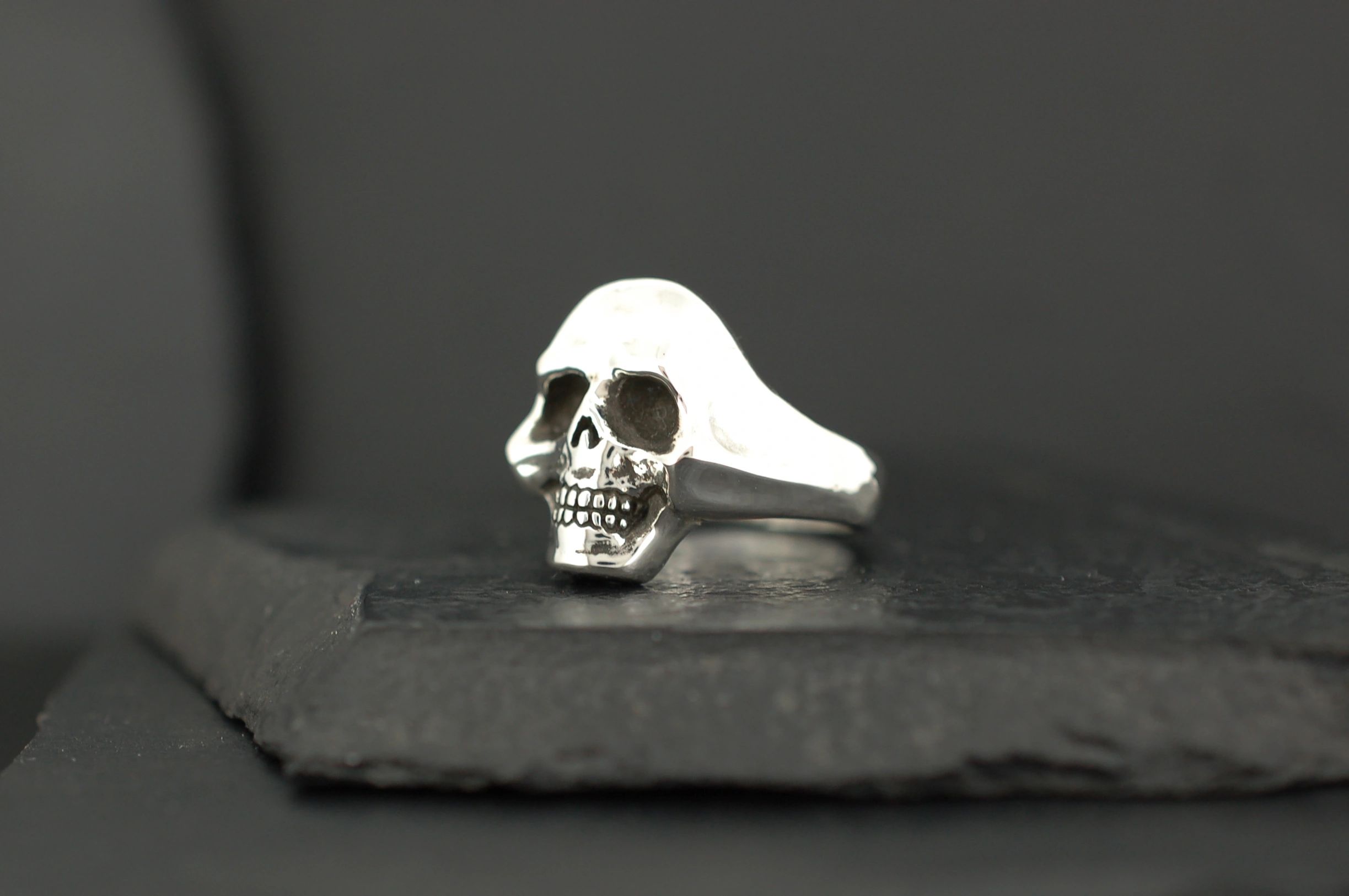 A silver ring featuring a detailed skull design on a dark surface.