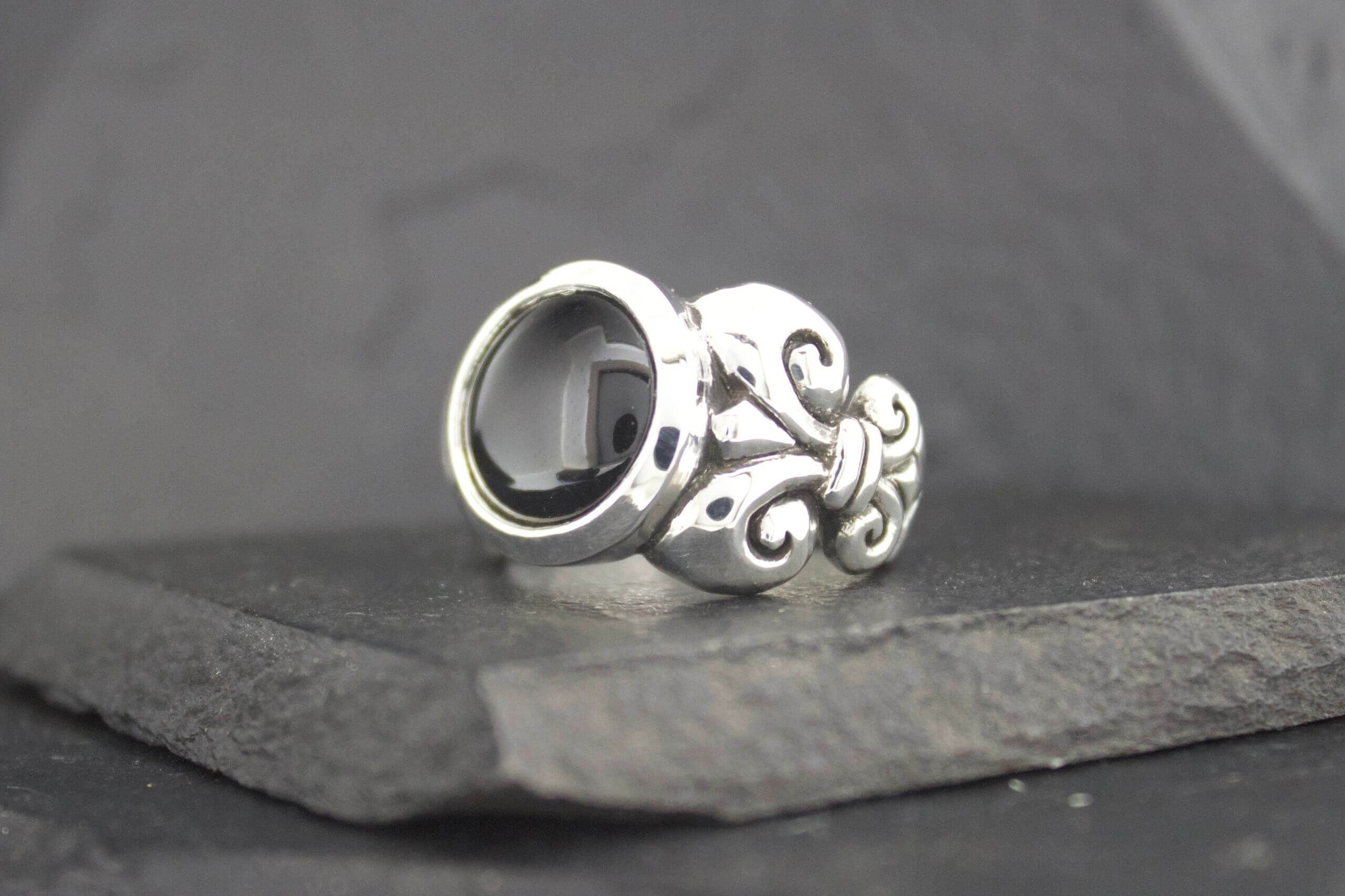 Ornate silver ring with an empty circular setting on a dark surface.