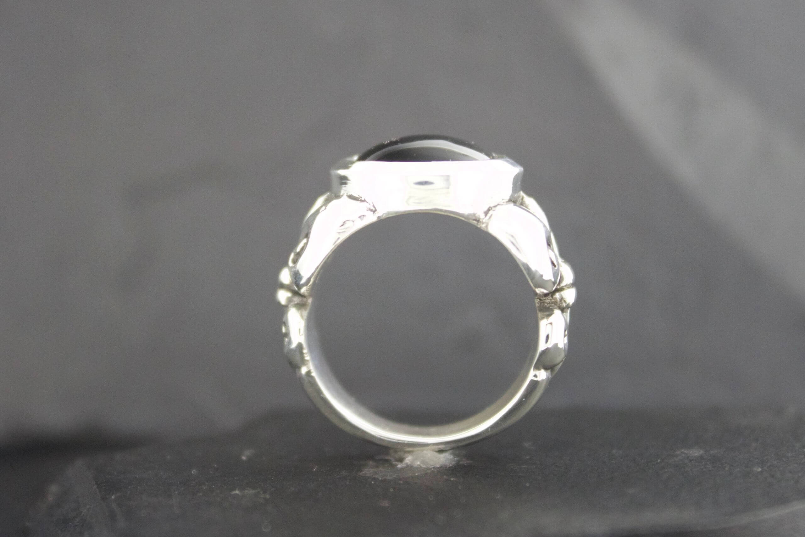 Close-up of a silver ring with an empty setting on a gray background.