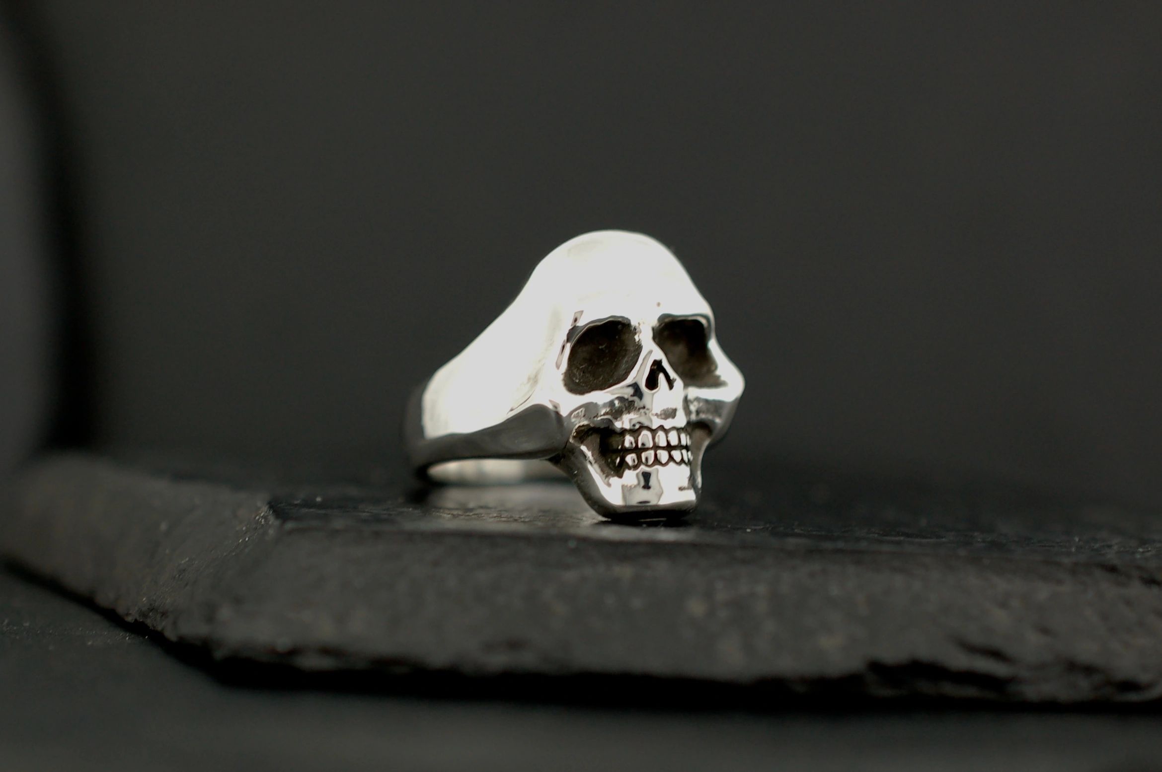 Silver skull-shaped ring on a dark surface.
