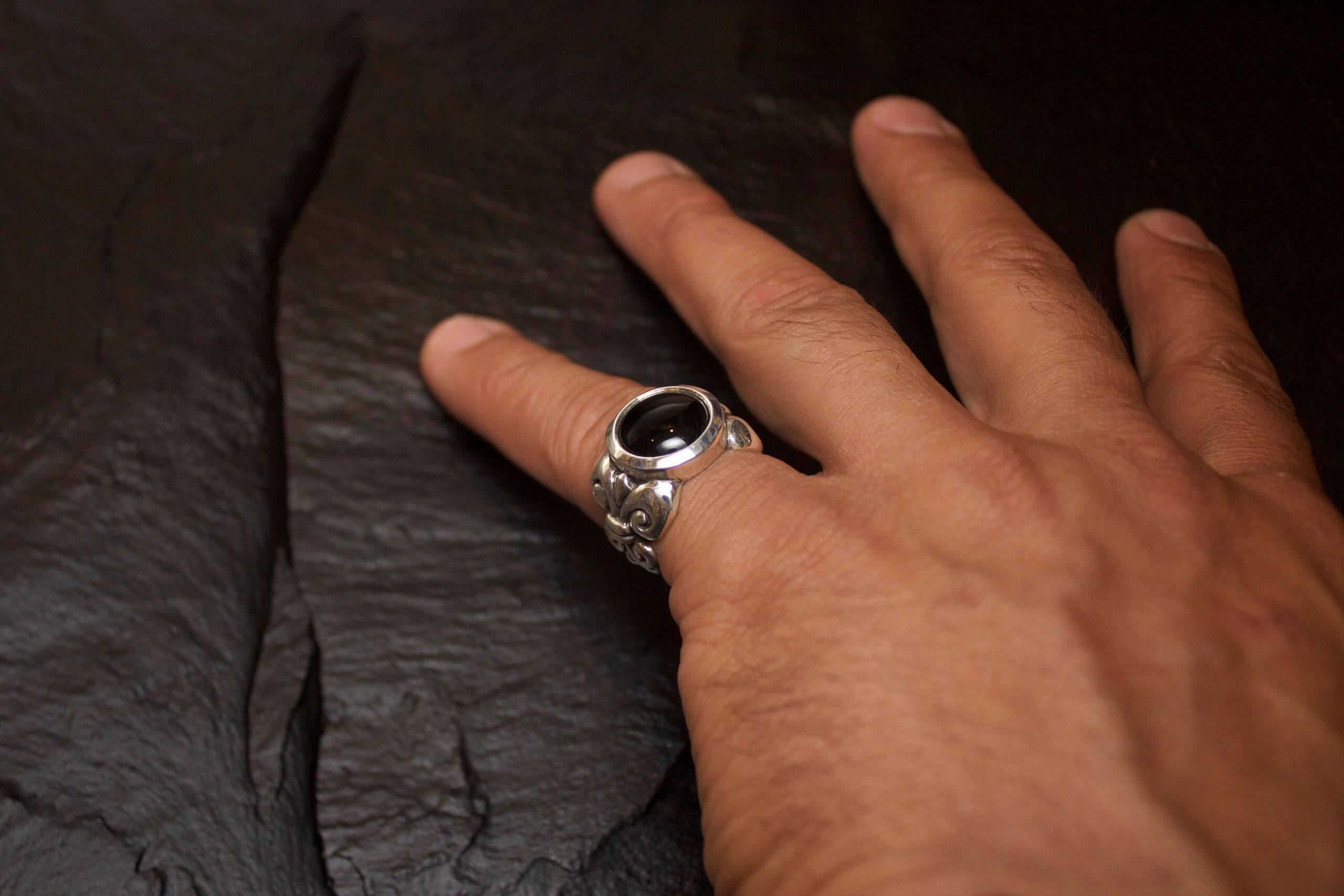 Hand wearing a silver ring with a black stone on a dark surface.